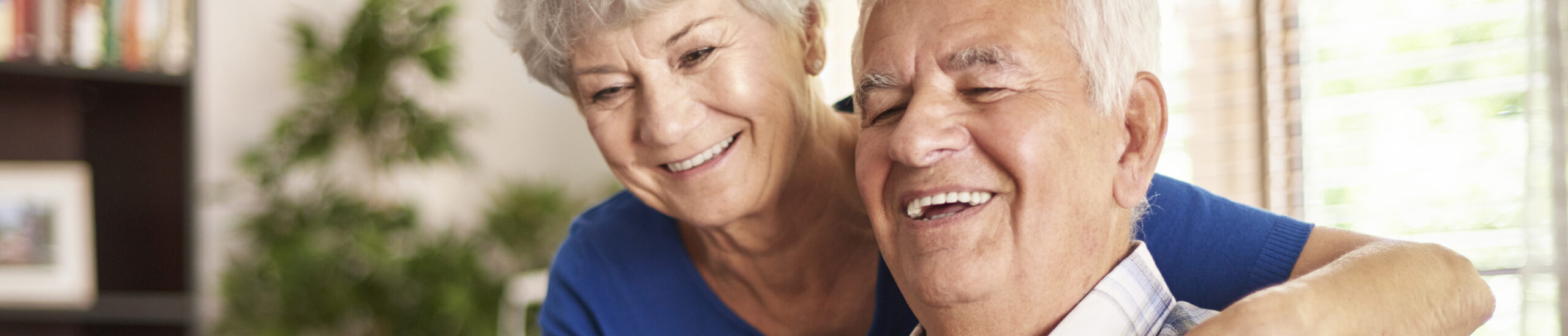Dos adultos mayores sonrientes y abrazándose y en el hogar