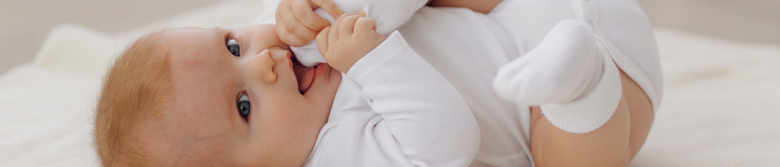 Bebé de ojos y acostado en cama mientras se agarra un pie