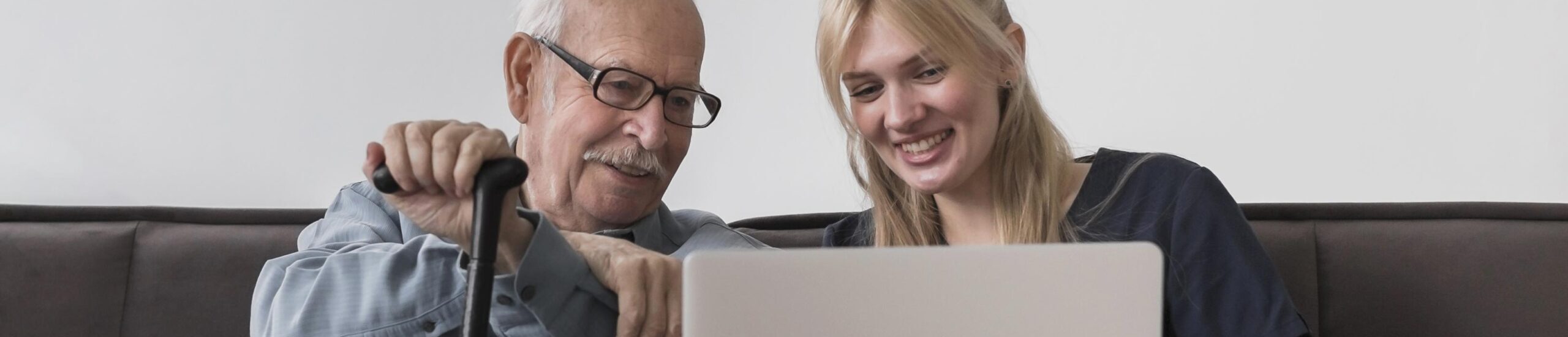 Hombre mayor con gafas señalando una pantalla mientras una chica rubia y joven ríe a su lado